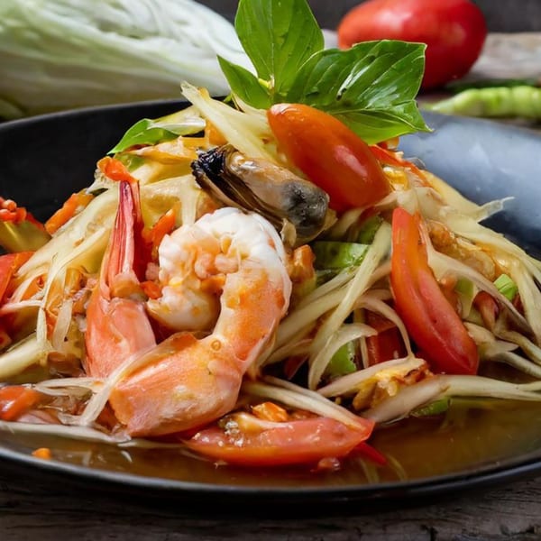 Som Tum, a Thai papaya salad with shrimp, mussels, tomatoes, and basil on a dark plate.