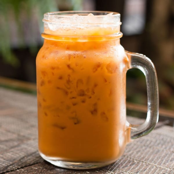 Iced Thai tea in a glass mason jar with a handle, on a woven placemat.
