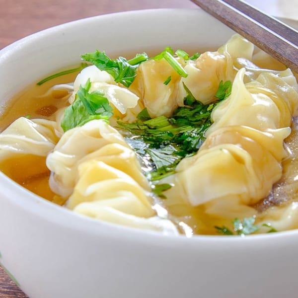 Close-up of a white bowl filled with Thai wonton soup, garnished with fresh cilantro and chopsticks.