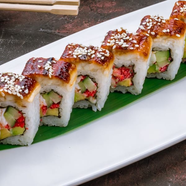 Dragon sushi rolls with eel, avocado, cucumber, and roe, topped with sesame seeds on a white plate.